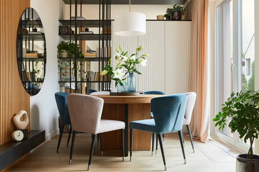 Modern dining area with a round wooden table, velvet chairs, and a floral centerpiece.