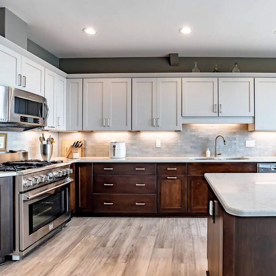 Modern kitchen with two-tone cabinets, stainless steel appliances, and marble countertops.