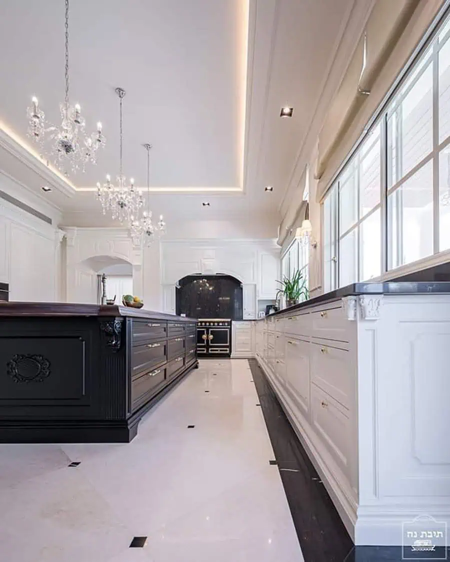 Luxurious kitchen with black island, white cabinetry, chandeliers, and polished marble floors.