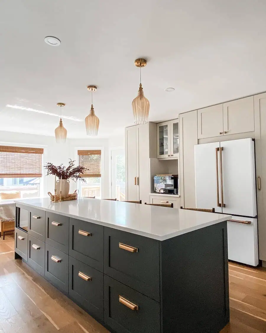 Modern kitchen with dark green island, brass hardware, and beige cabinetry with pendant lights.