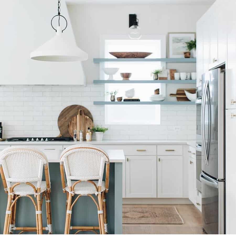 Bright kitchen with white cabinets, blue open shelves, and rattan bar stools.