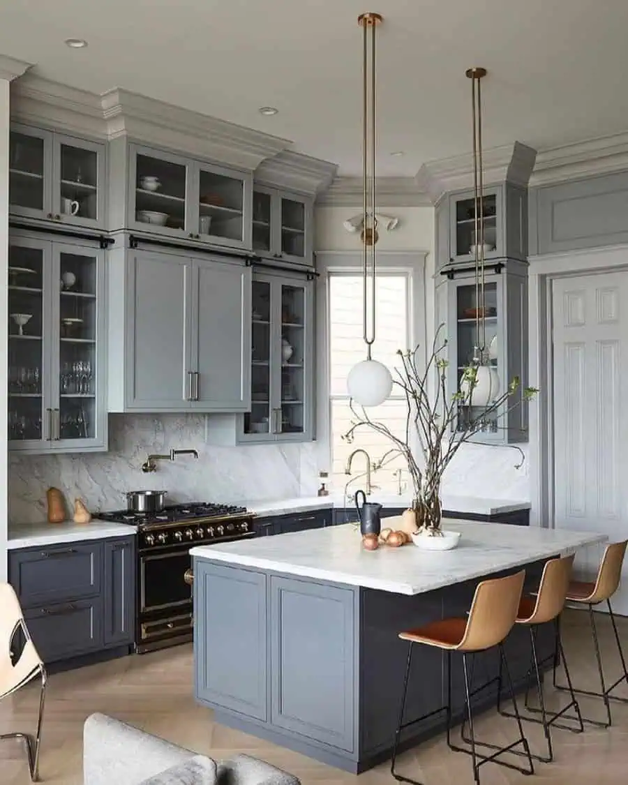 Elegant kitchen with gray cabinets, marble backsplash, and brass accents on lighting and fixtures.