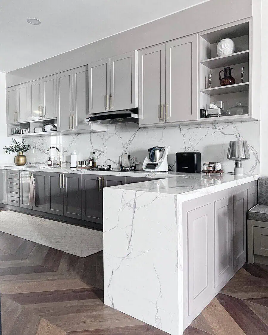 Modern kitchen with light and dark gray cabinets, marble countertops, and herringbone flooring.