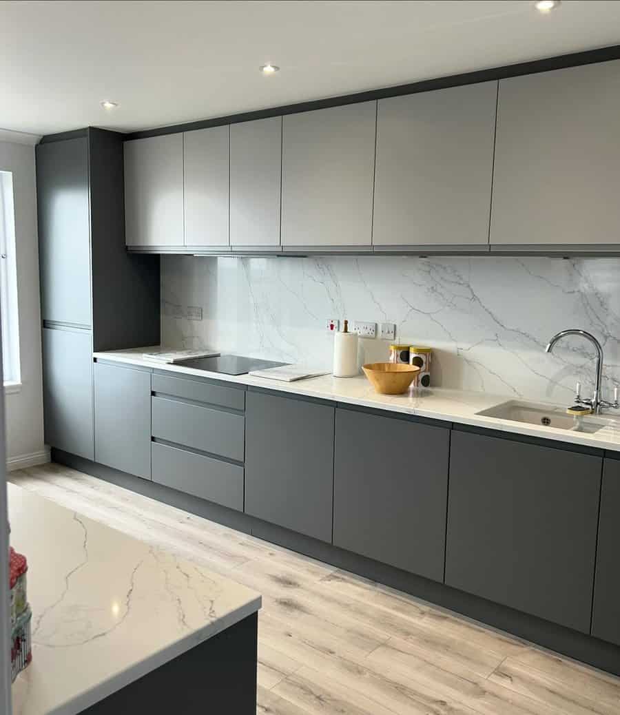 Sleek kitchen with matte gray cabinets, marble backsplash, and light wood flooring.