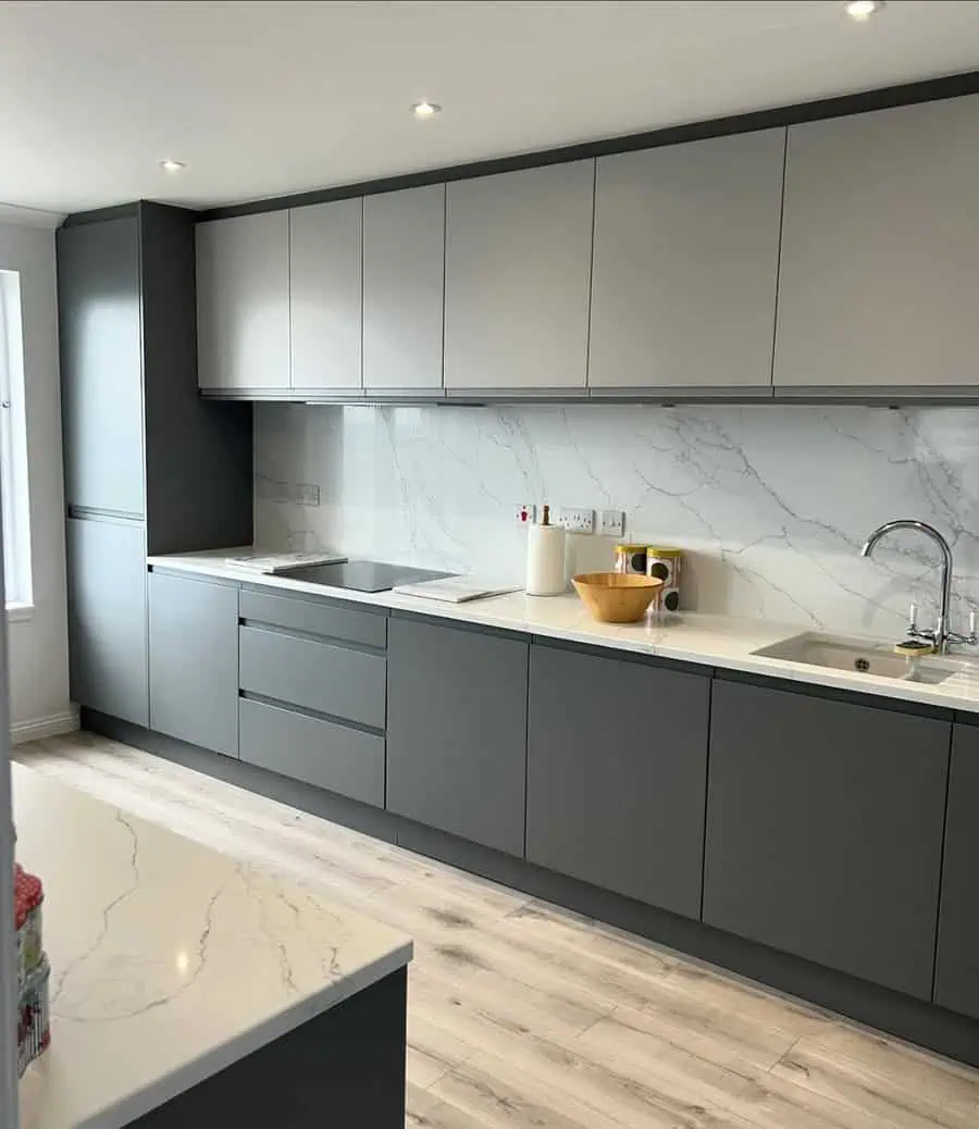 Sleek kitchen with matte gray cabinets, marble backsplash, and light wood flooring.