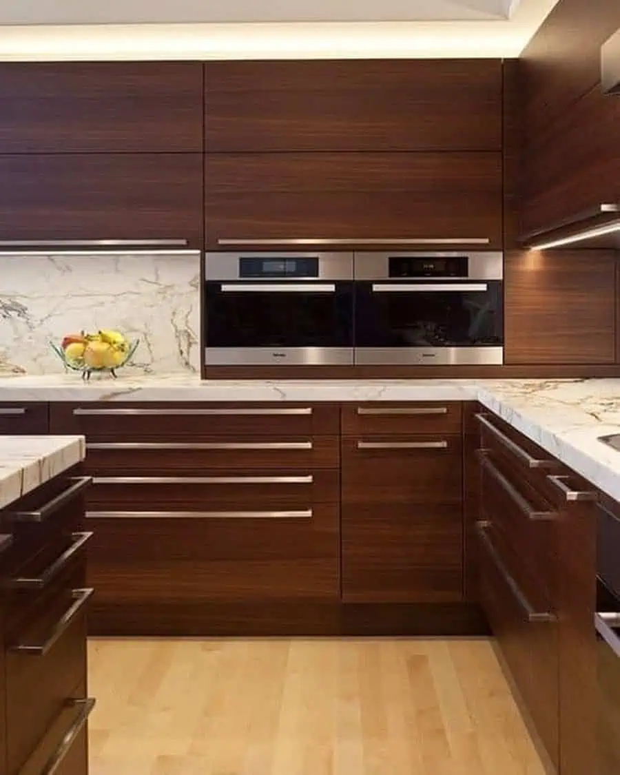 Modern kitchen with rich wood cabinets, marble backsplash, and built-in stainless steel appliances.