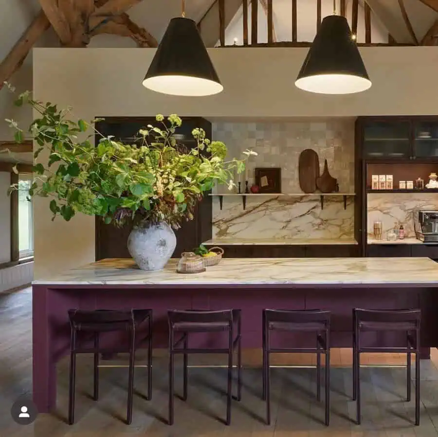 Rustic kitchen with maroon island, marble countertop, and exposed wooden beams.