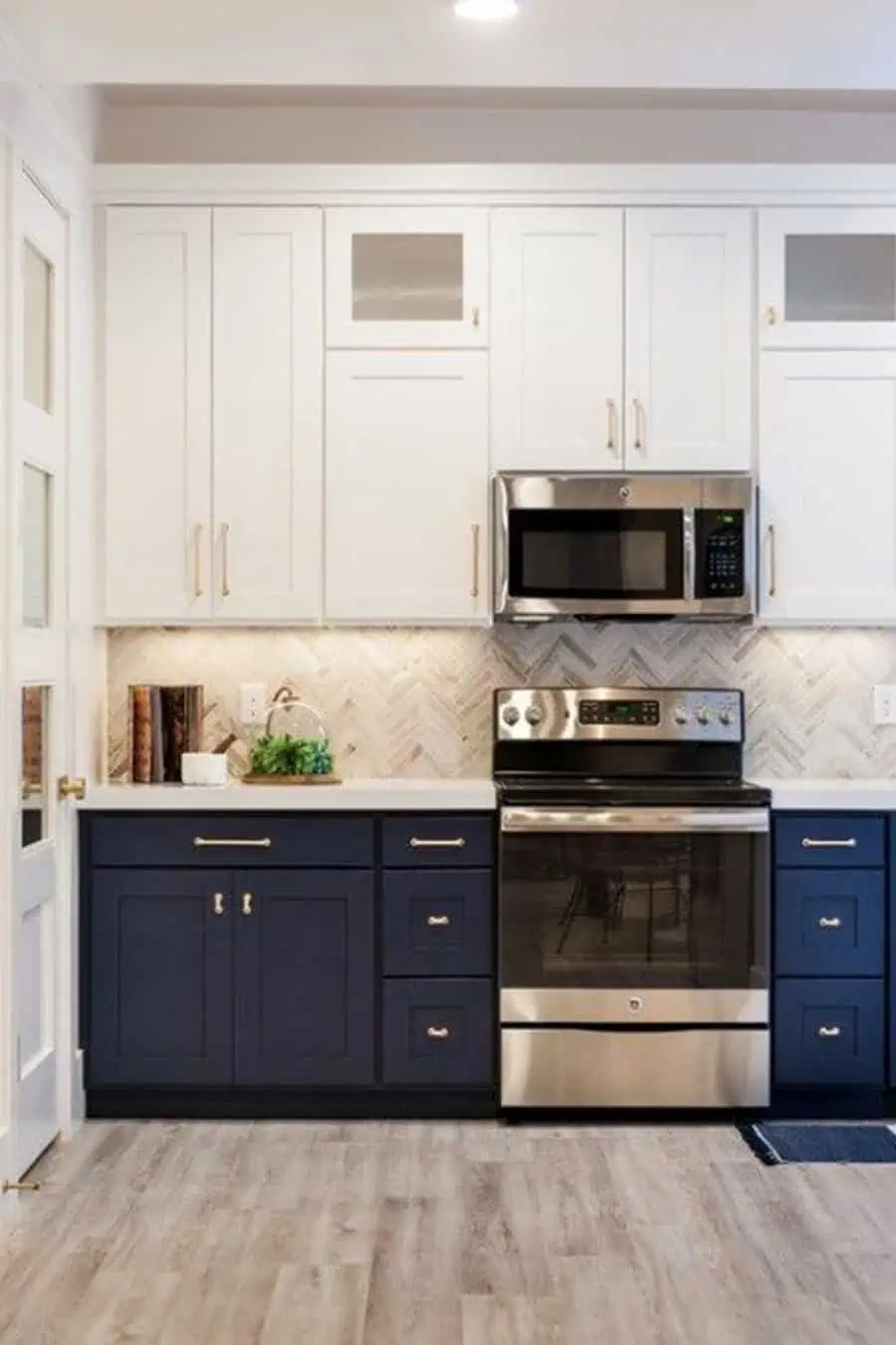 Two-tone kitchen with navy lower cabinets, white uppers, and a herringbone backsplash.