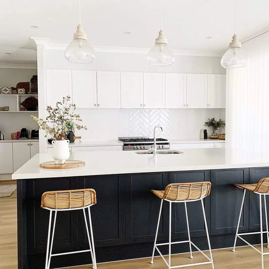 Bright and modern kitchen featuring white upper cabinets, contrasting black lower cabinets, wicker bar stools, and glass pendant lights.