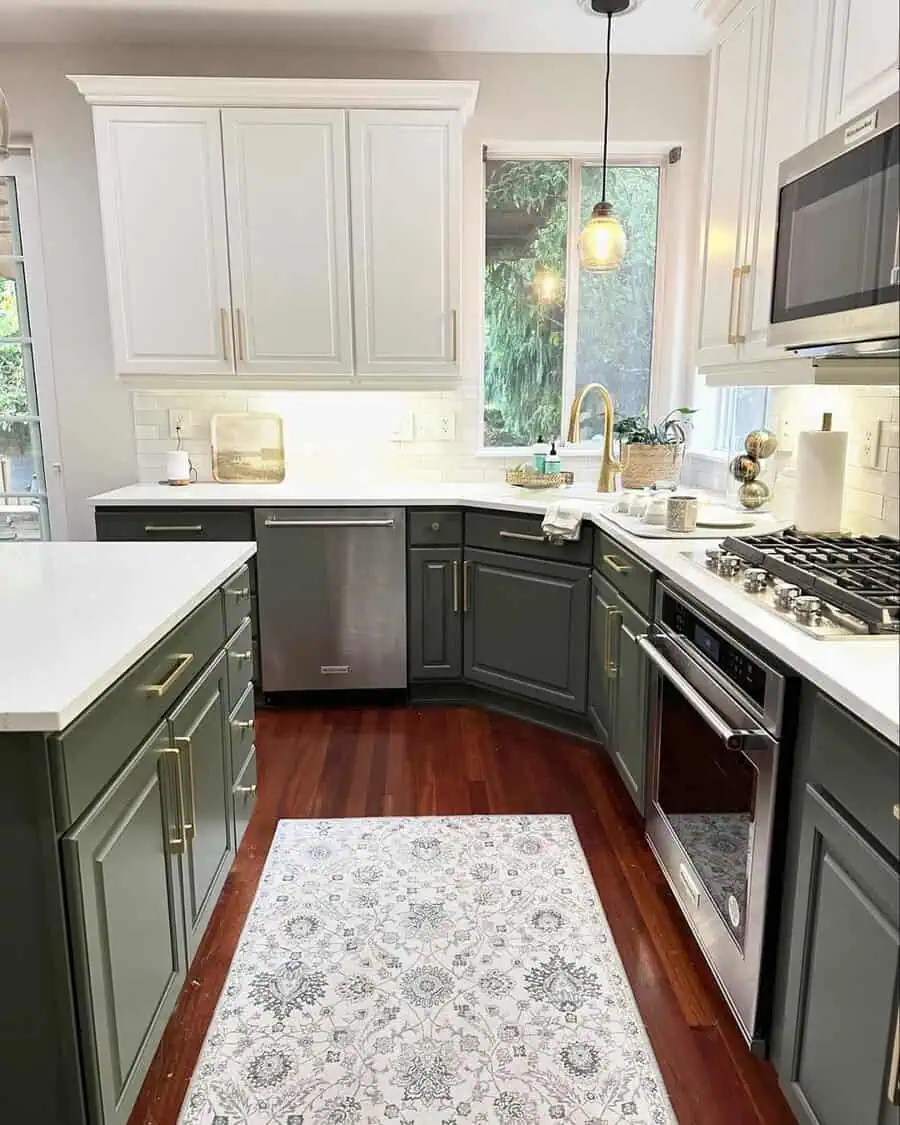 A stylish two-tone kitchen with white and sage green cabinets, accented by gold hardware and natural light.