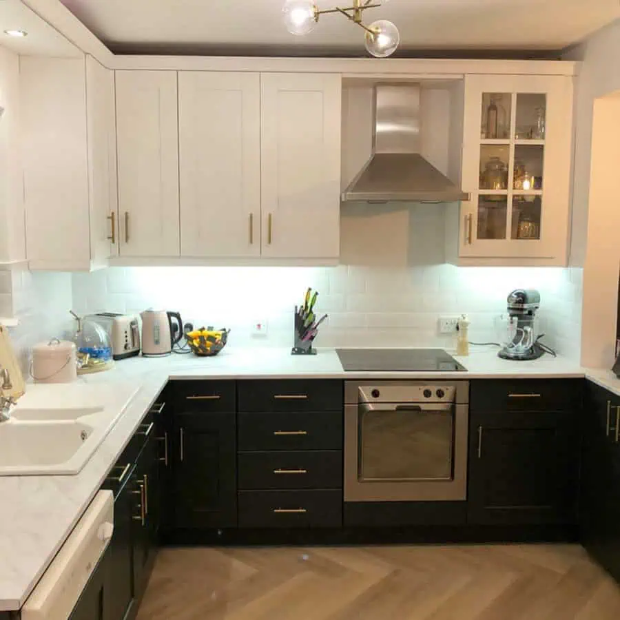 A modern two-tone kitchen with white upper cabinets, black lower cabinets, and gold accents for contrast.