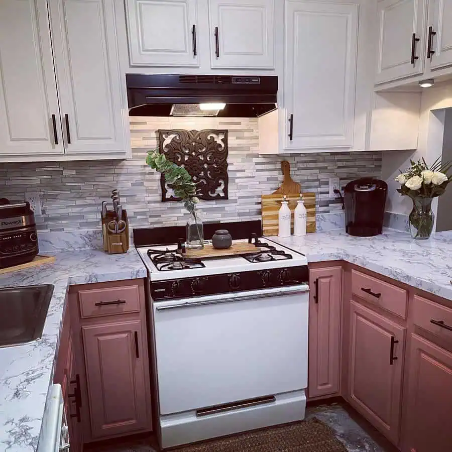 A two-tone kitchen with white upper and pink lower cabinets, marble-style countertops, and a mosaic backsplash.