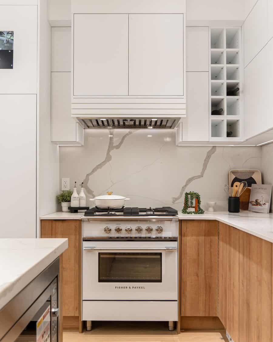 Compact kitchen with white upper cabinets, wood lower cabinets, and a marble backsplash.