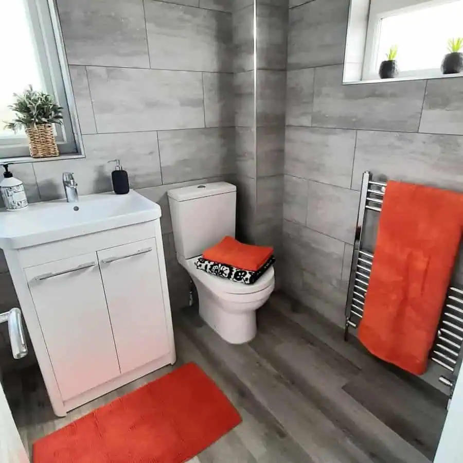 Bathroom with wood-look grey floor tiles, grey wall tiles, and orange towel accents.