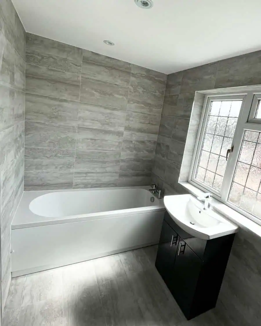 Bathroom with grey wood-look floor tiles, matching wall tiles, and a modern white bathtub.