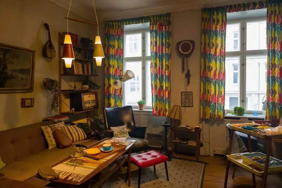 Retro 1960s living room with colorful curtains, vintage furniture, and a cozy seating area.