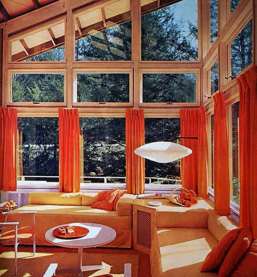 1960s sunroom with floor-to-ceiling windows, bold orange decor, and a retro sectional sofa.