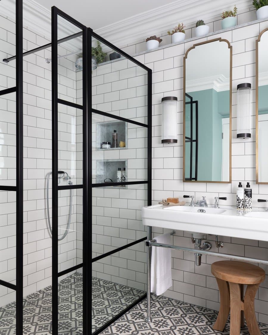 Black and white bathroom with Art Deco mirrors, patterned floor tiles, and a glass shower enclosure.