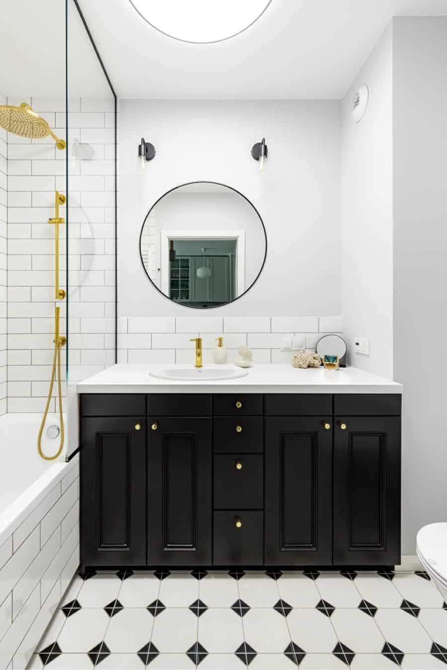 Black and white bathroom with gold accents, subway tiles, and a round mirror.
