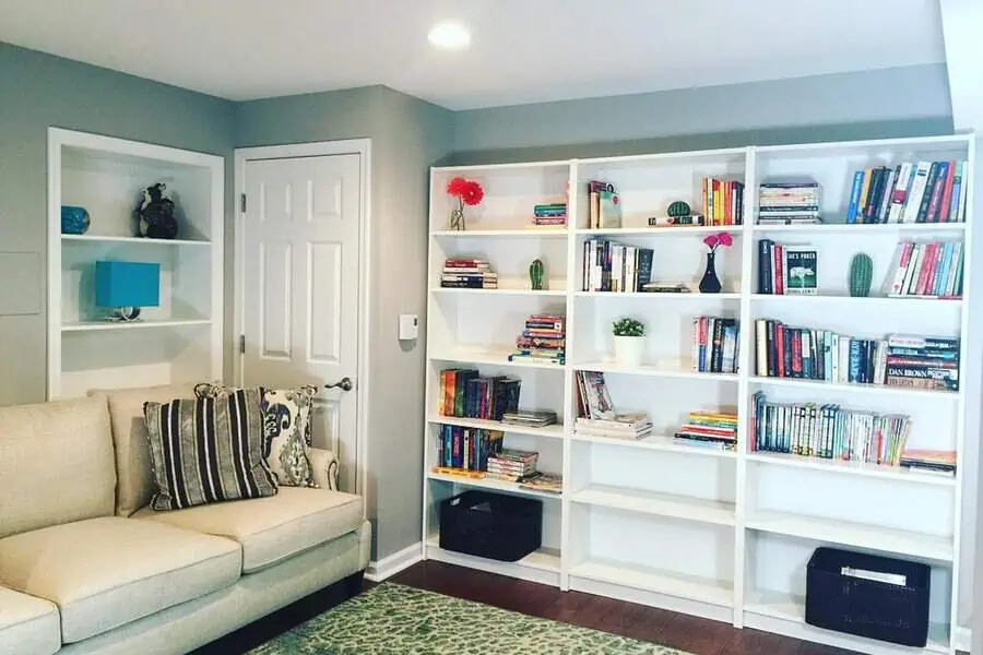 Basement home library with white bookshelves, cozy seating, and soft lighting.