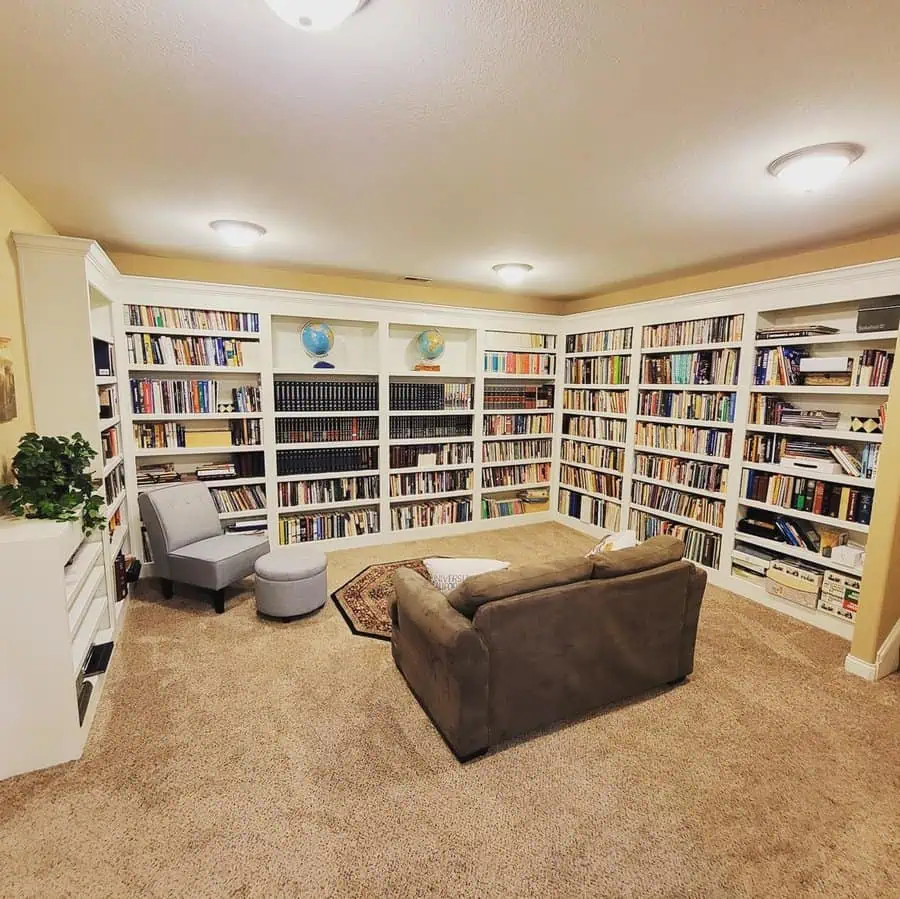 Basement home library with built-in white bookshelves, plush seating, and soft lighting.