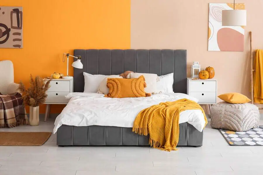 Bedroom with two-tone walls in bold orange and soft neutrals, cozy bedding, and warm decor accents.