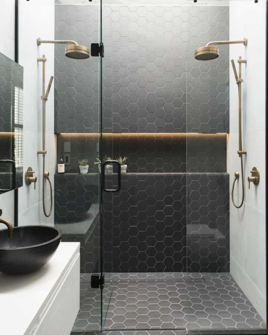 Black and white bathroom with a black hexagon tile accent wall, gold fixtures, and a glass shower.