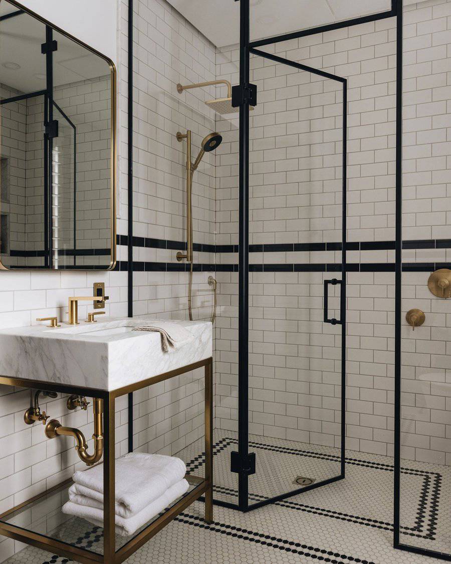 Black and white bathroom with classic subway tiles, gold fixtures, and a glass shower enclosure.