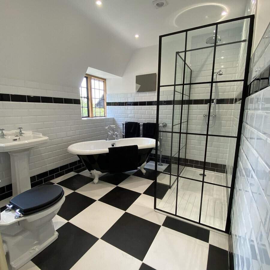 Black and white bathroom with checkerboard flooring, clawfoot tub, and glass shower enclosure.