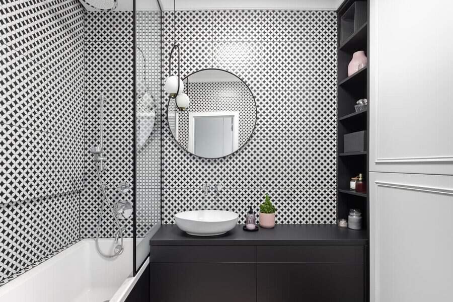 Black and white bathroom with geometric wall tiles, round mirror, and modern vanity.