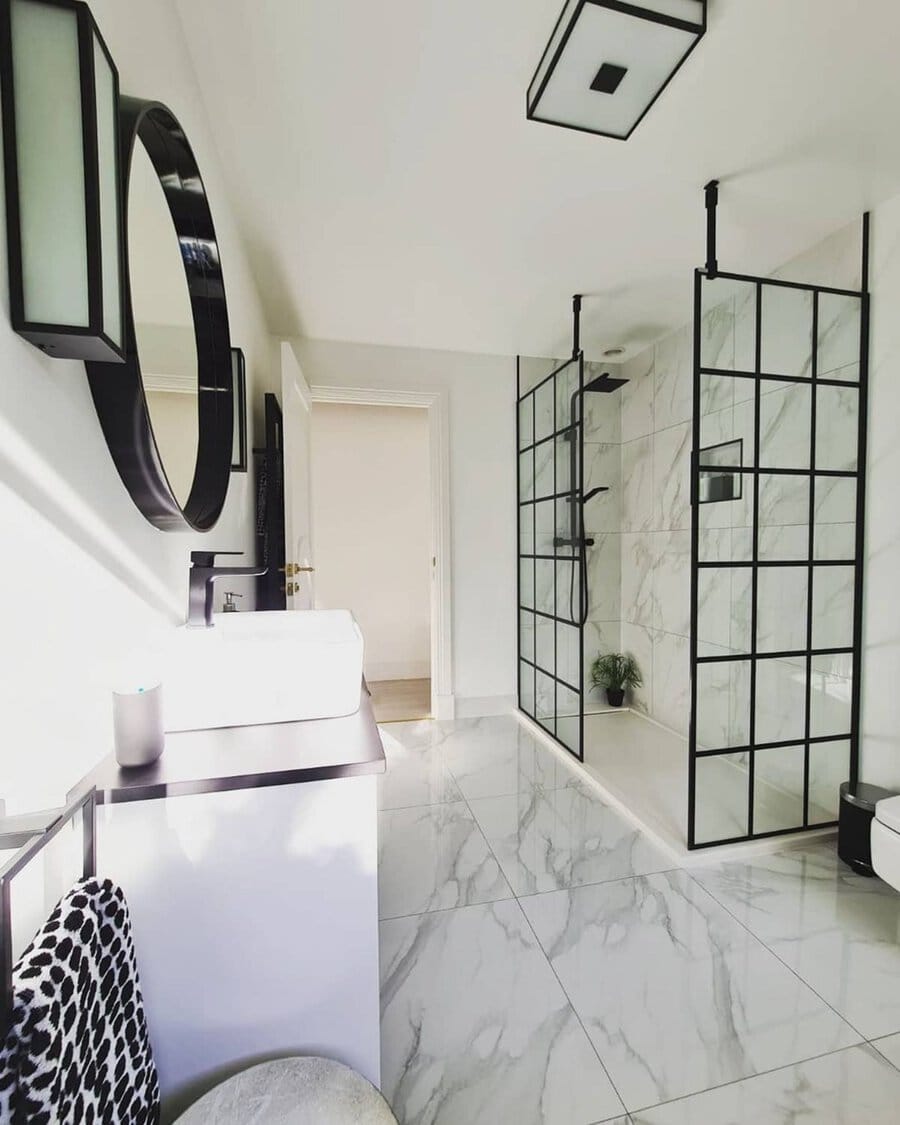 Modern black and white bathroom with marble flooring, grid glass shower, and sleek black accents.