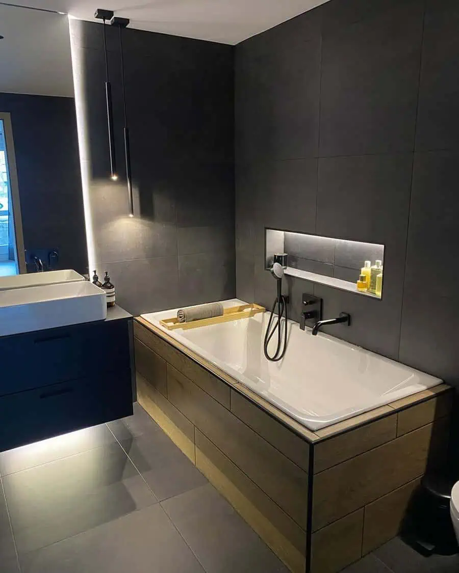 Modern black bathroom with wood-accented bathtub, ambient lighting, and sleek fixtures.