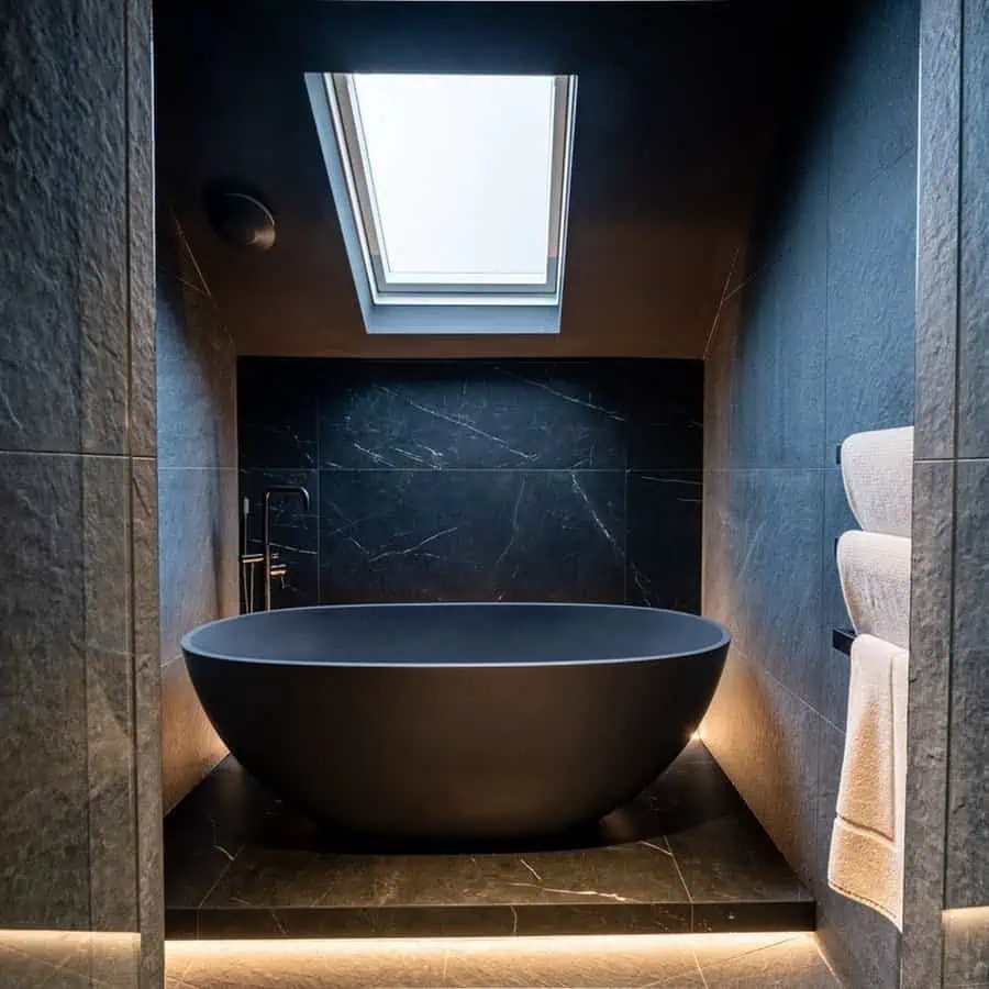 Luxury black bathroom with a freestanding tub, skylight, and ambient floor lighting.