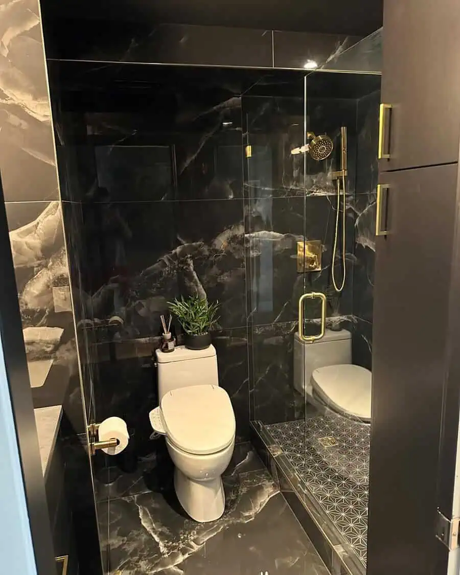 Luxurious black bathroom with marble walls, gold fixtures, and a glass-enclosed shower.