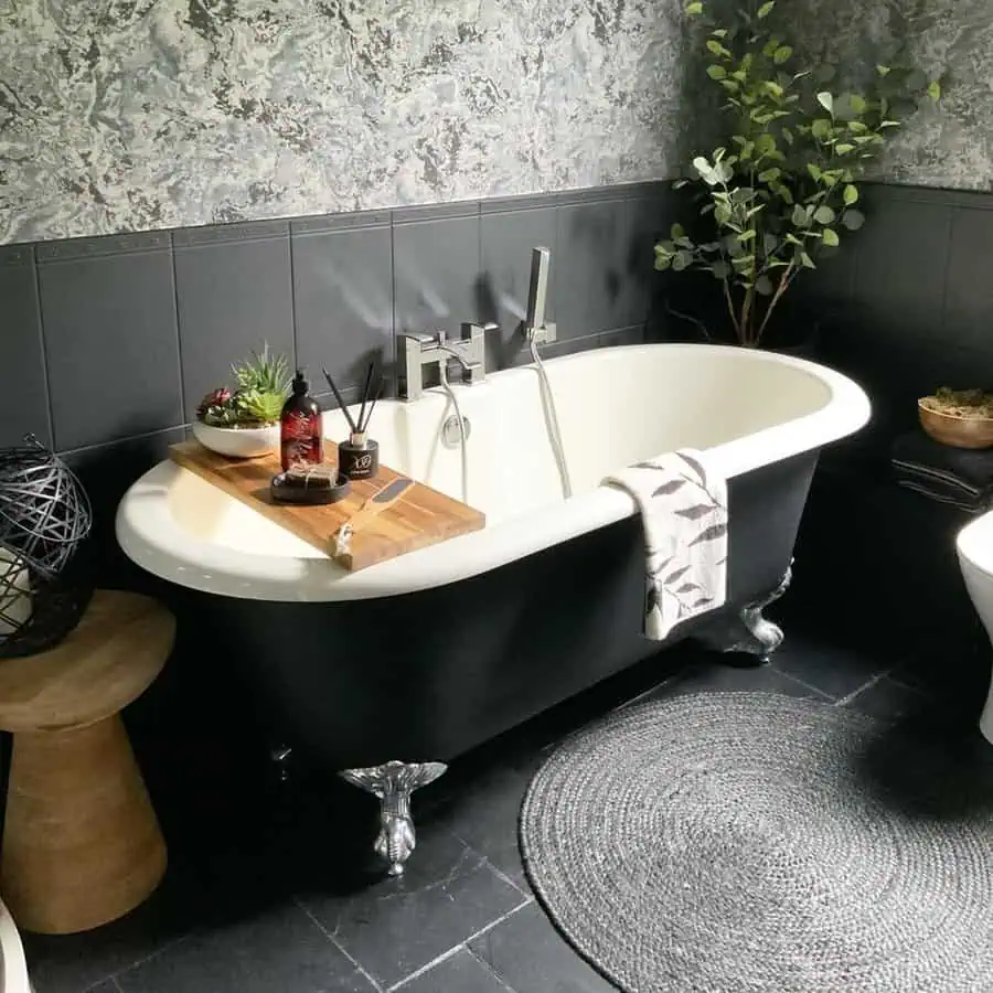 Cozy black bathroom with a clawfoot tub, textured rug, and soft decorative textiles.