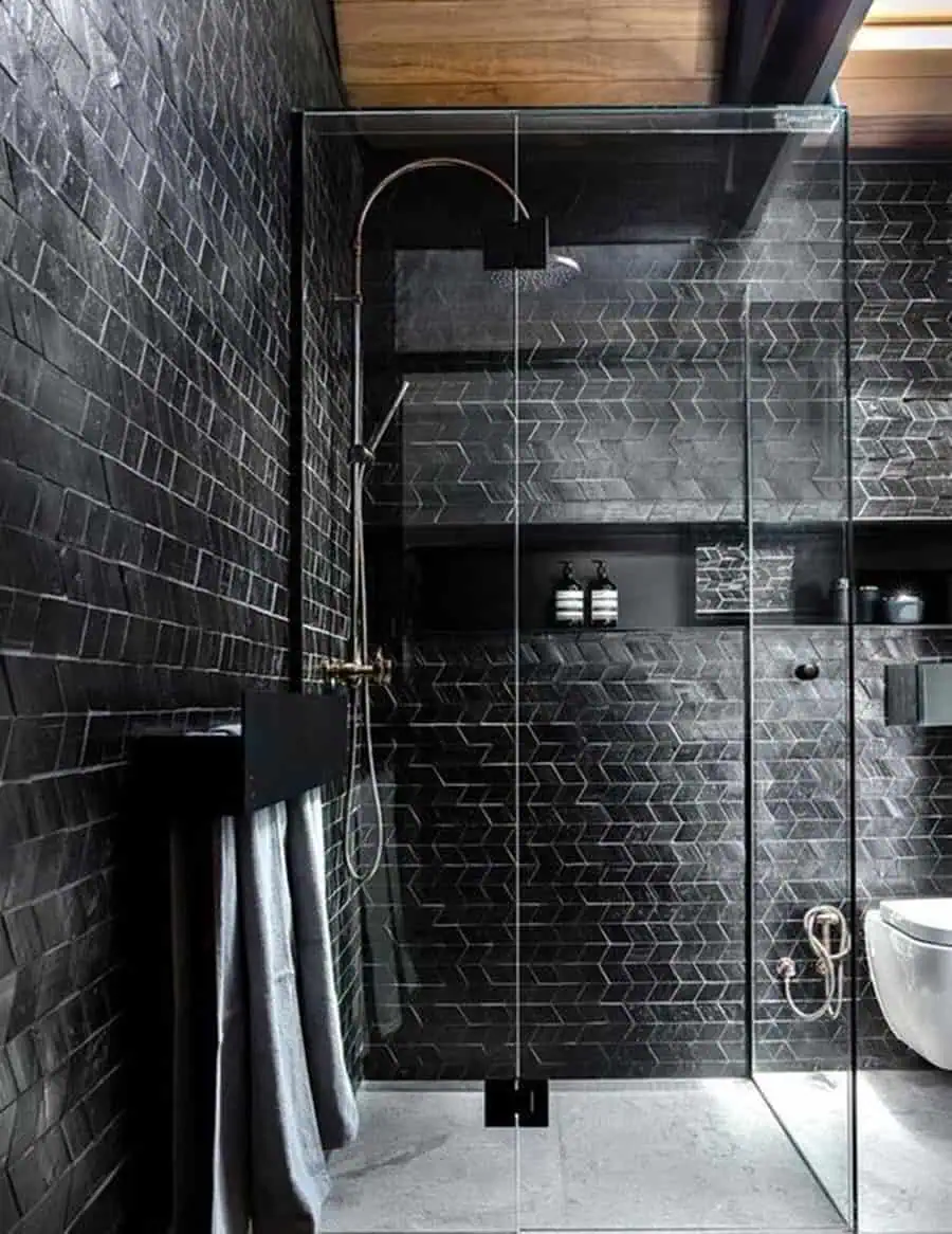 Rustic black bathroom with textured tiles, glass shower enclosure, and wood ceiling accents.