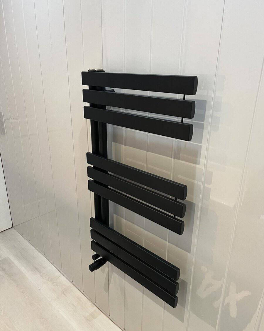 Modern black towel rail mounted on white paneled bathroom wall.