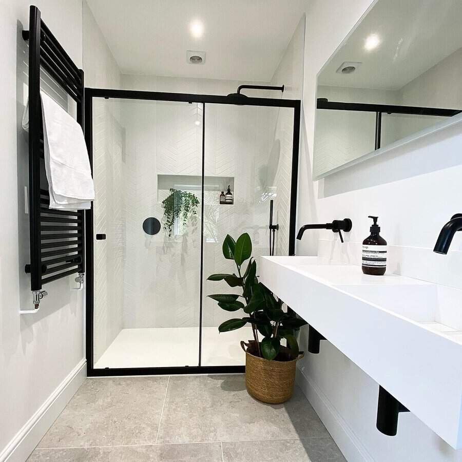 Minimalist black and white bathroom with a glass shower, black towel rail, and greenery accents.