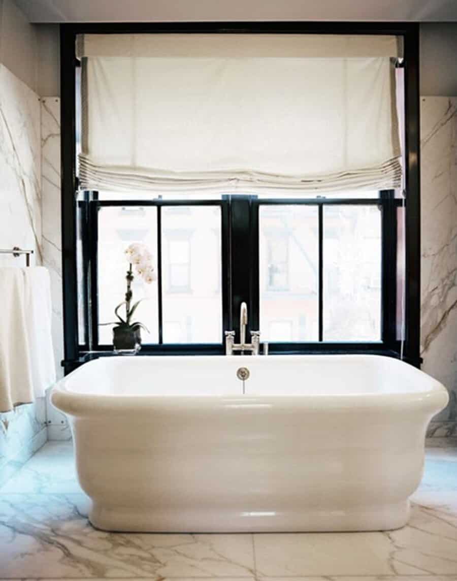 Black and white bathroom with black trim windows, marble flooring, and a freestanding bathtub.