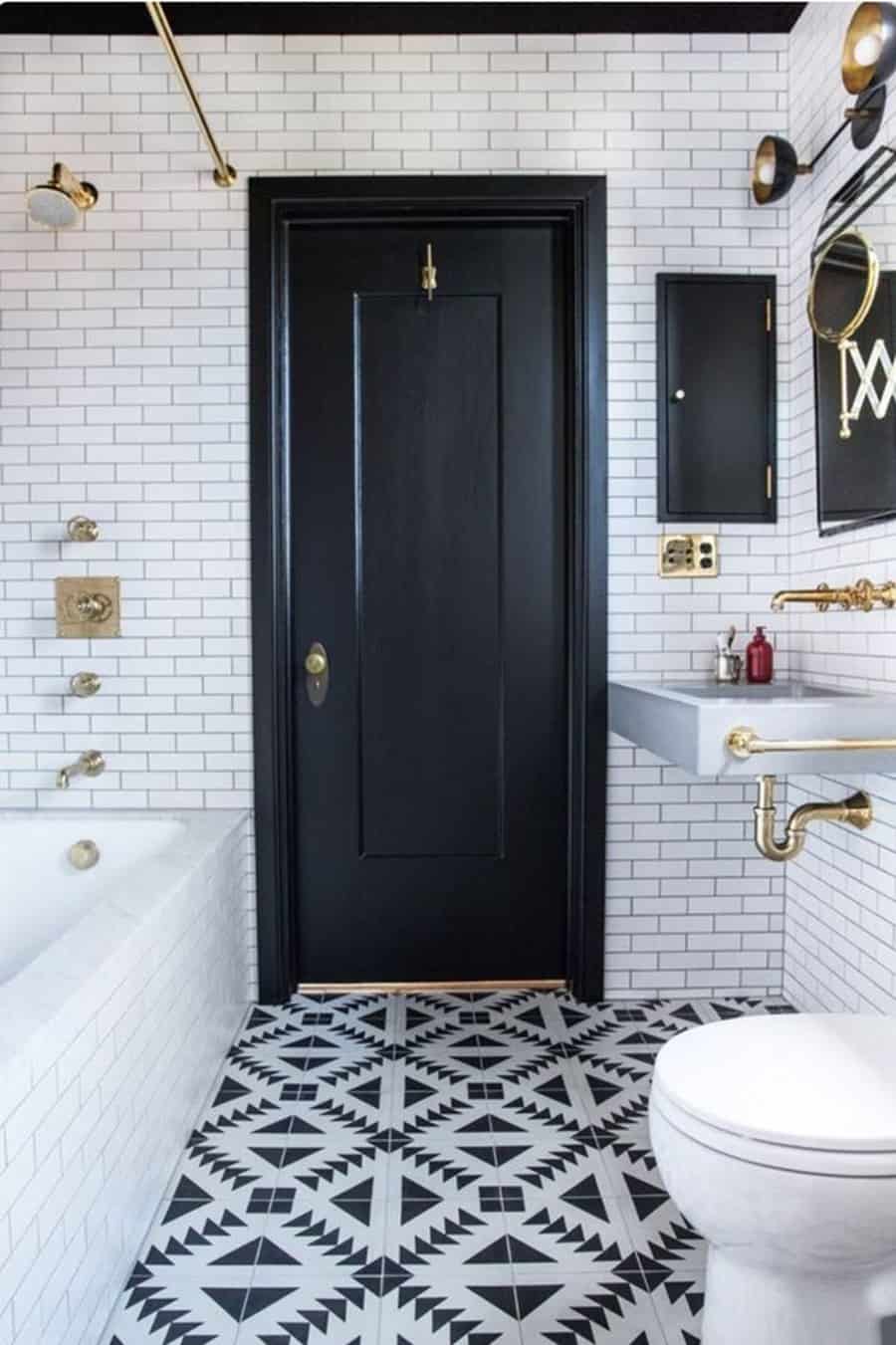 Black and white bathroom with geometric floor tiles, gold fixtures, and a bold black door.