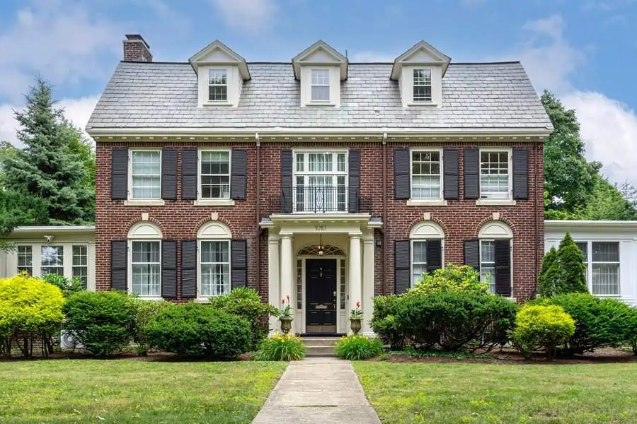 Brick Dutch Colonial house with dormer windows, black shutters, and a classic symmetrical facade.