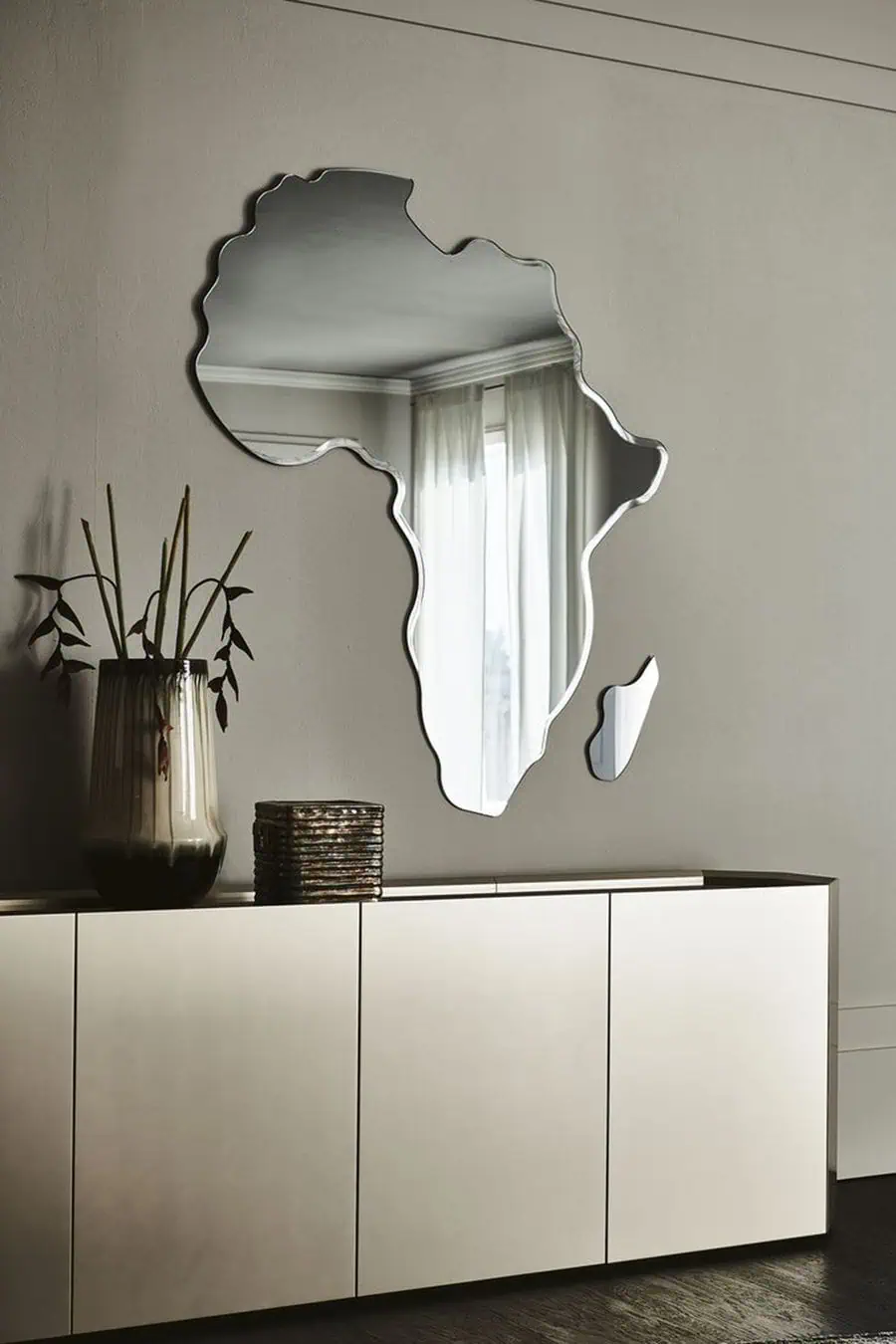 Africa-shaped wall mirror above a sleek sideboard in a modern, minimalist living room.