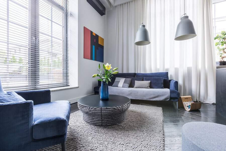Carpeted living room with a blue sofa, modern decor, and a textured area rug.