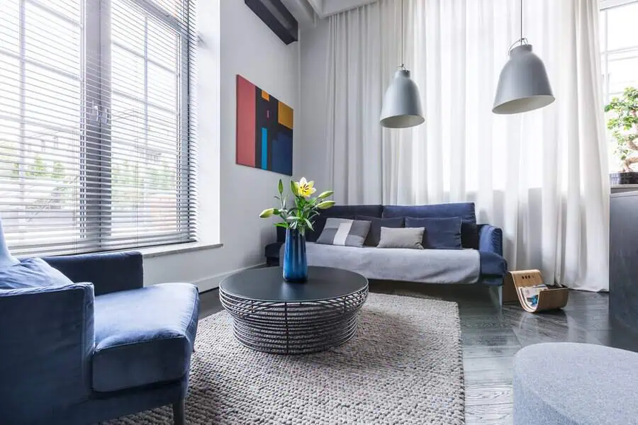 Carpeted living room with a blue sofa, modern decor, and a textured area rug.