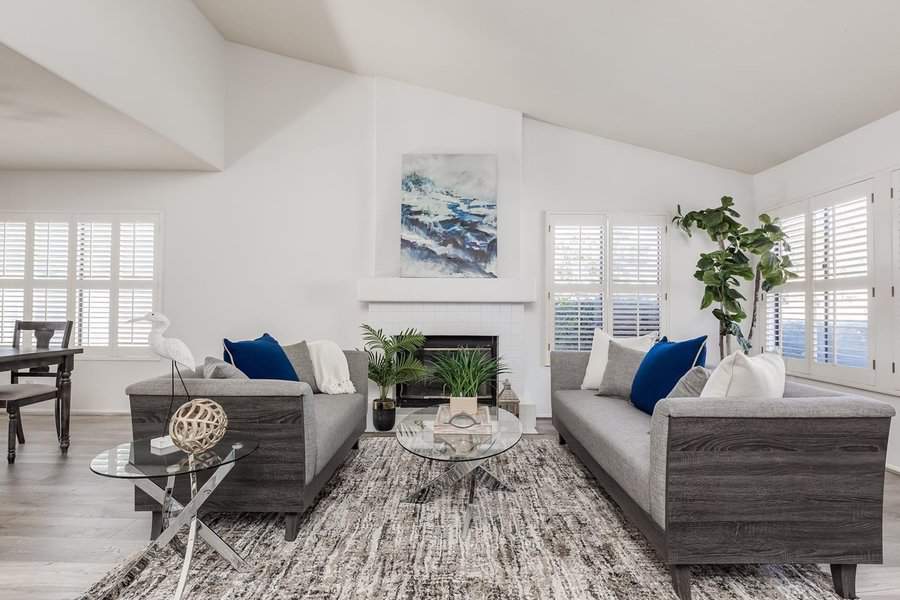 Carpeted living room with grey sofas, a glass coffee table, and a fireplace centerpiece.