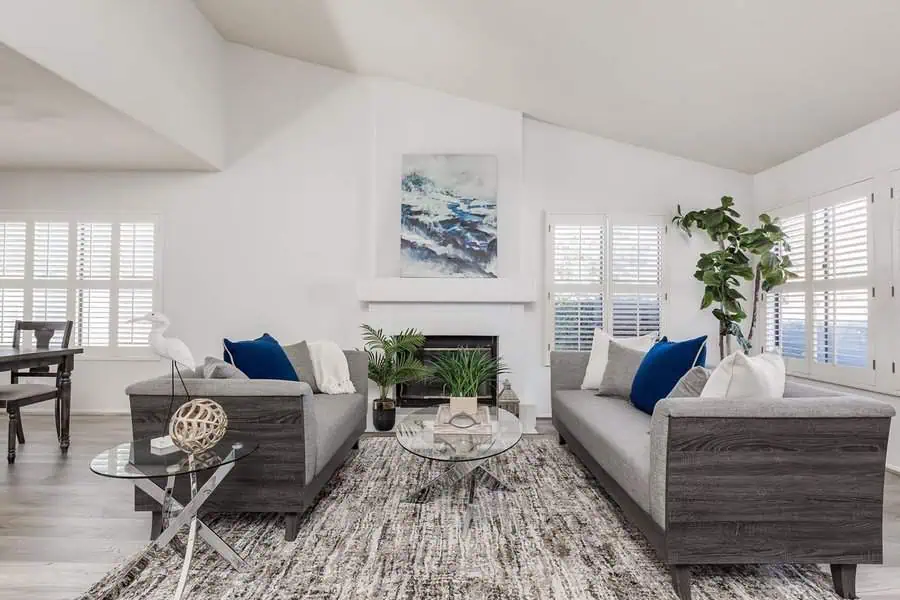 Carpeted living room with grey sofas, a glass coffee table, and a fireplace centerpiece.