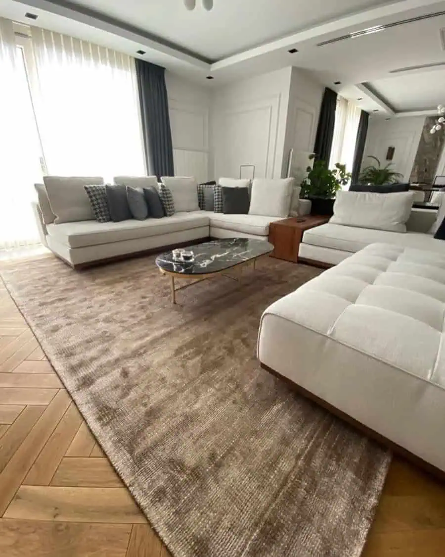 Carpeted living room with white sectional sofas, a marble coffee table, and elegant decor.