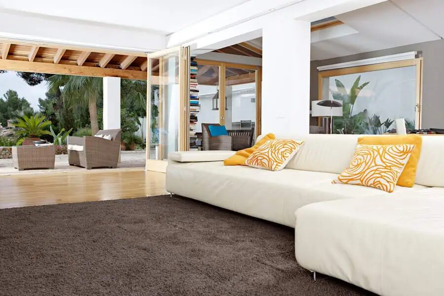 Carpeted living room with a white sectional sofa, brown rug, and open patio view.