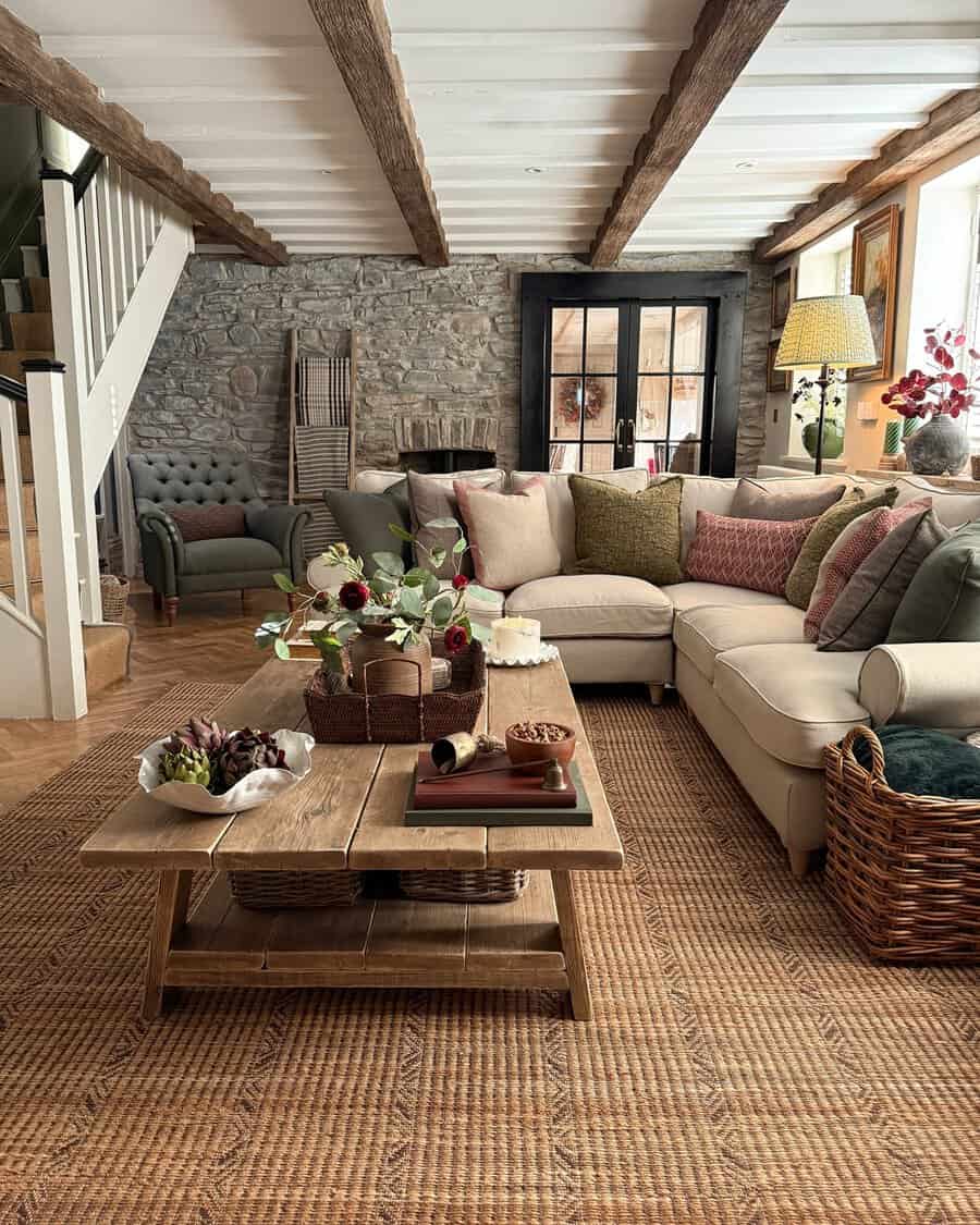 Cozy carpeted living room with a rustic wood-beamed ceiling, stone wall, and sectional sofa.