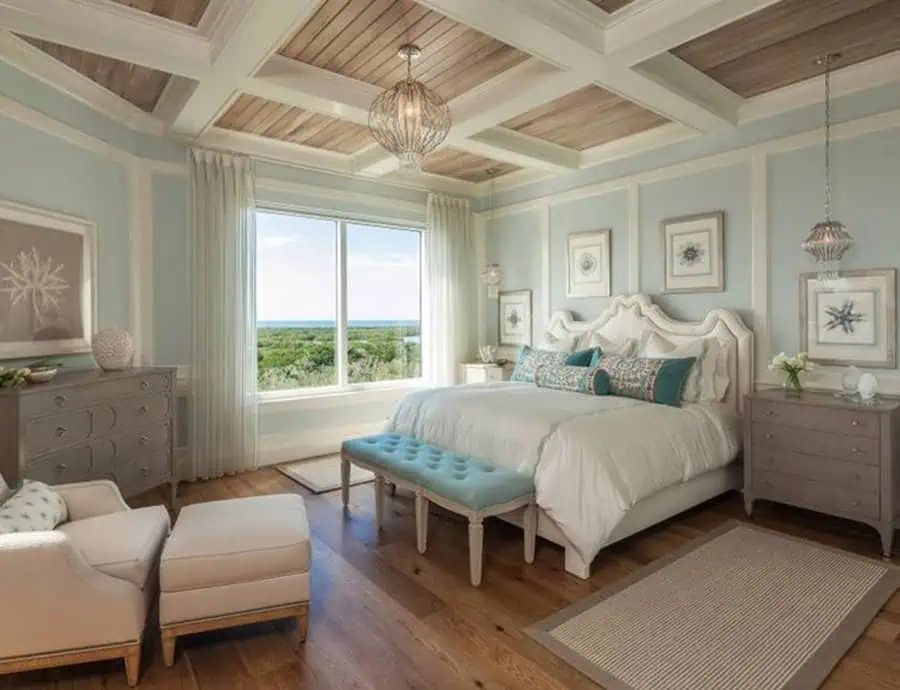 Coastal bedroom with a modern coffered ceiling, soft blue walls, elegant decor, and ocean views.